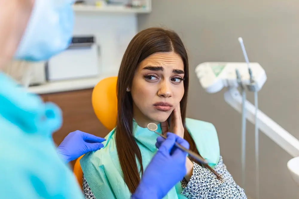 Woman holding cheek with toothache in chair at dentist