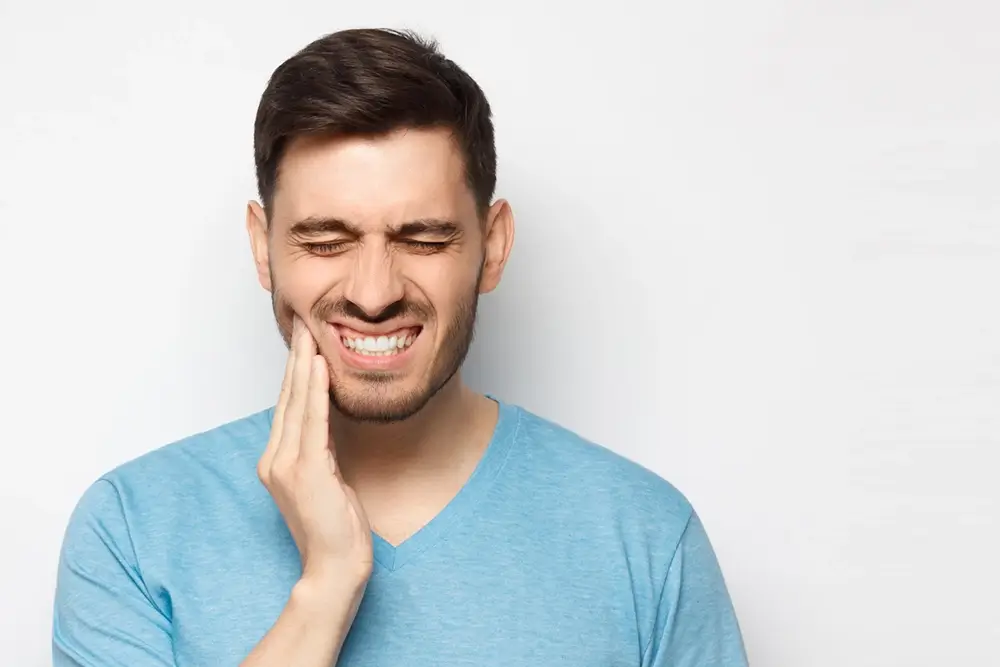 Man in blue tshirt touching his face and closing eyes with painful expression from aching tooth
